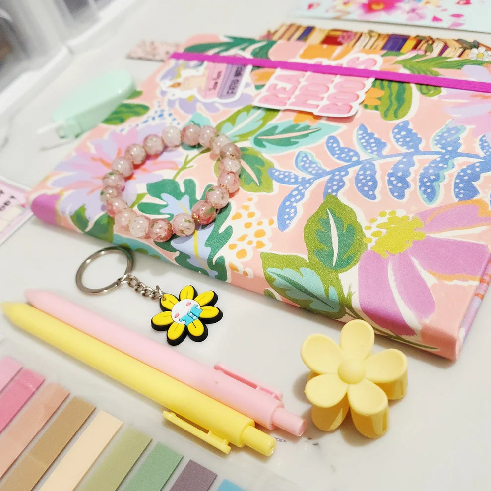 Floral notebook, pens, keychain, and flower-shaped items on a white surface